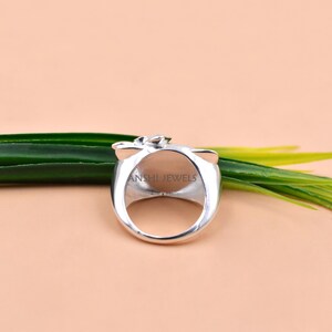 May include: A silver-toned ring featuring a smooth, rounded band and a decorative top element. The interior of the ring band is clearly engraved with the text ANSHI JEWELS in a clean, sans-serif font, visible through the open center of the ring.