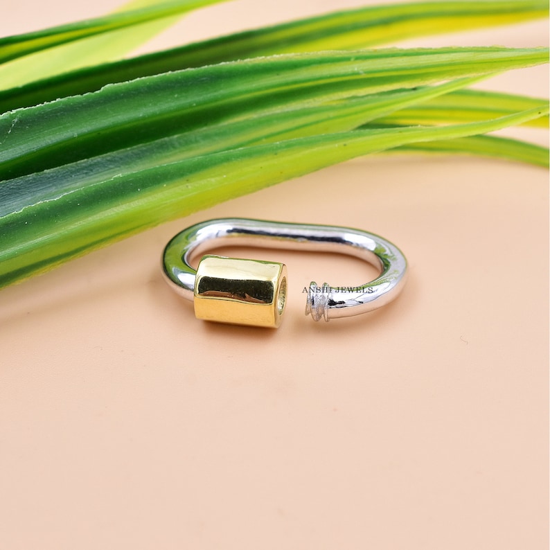 May include: A silver and gold oval-shaped ring with a textured design. The ring is made of two different metals, with a gold band on one side and a silver band on the other.