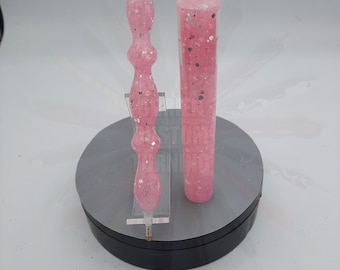 May include: Two pink resin pens with silver glitter. One pen is a straight tube shape and the other is a bulbous shape with a pointed tip.
