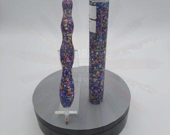 May include: Two colorful pens with a speckled pattern in shades of blue, purple, green, and gold. The pen on the left is a twist pen and the pen on the right is a straight pen. Both pens are on a rotating display stand.