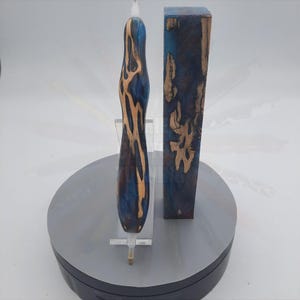 May include: A blue and brown wooden pen blank with a natural wood grain pattern. The blank is shown next to a finished pen made from the same wood.