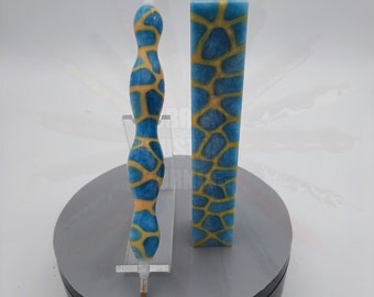 May include: A blue and yellow patterned pen and a block of the same pattern. The pen is on a white stand and the block is on a gray circular surface.