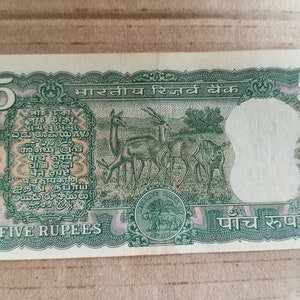 May include: A five-rupee Indian banknote with a green and pink design. The note features deer grazing in a field, text in multiple languages, and the words "FIVE RUPEES". The number "5" appears on both sides.