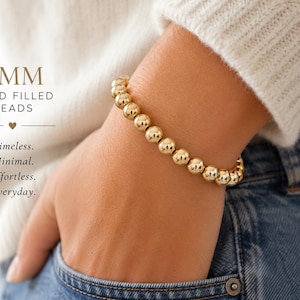 May include: Gold-filled bead bracelet with 8mm beads. The bracelet is shown on a wrist, with the text "Timeless. Minimal. Effortless. Everyday." in the image. The bracelet is a simple, elegant piece of jewelry.