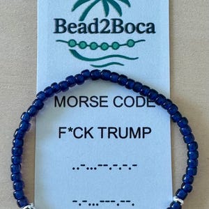 May include: A dark blue beaded bracelet with silver accents is displayed in front of a card. The card reads "MORSE CODE F*CK TRUMP" and includes the Morse code translation. The brand name "Bead2Boca" is at the top.