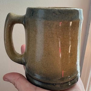 May include: A brown ceramic mug with a light blue glaze. The mug has a handle and a rounded base.