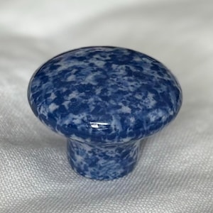 May include: A round cabinet knob featuring a glossy finish with a mottled blue and white pattern. The knob has a smooth, domed top surface that tapers down to a cylindrical base, creating a uniform speckled appearance across the entire object.
