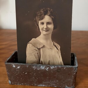 May include: A vintage photo of a woman in a light-colored dress is displayed in a rustic, brown metal picture frame.
