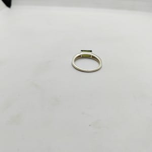 May include: A silver ring featuring a rectangular, light green gemstone. The ring band is a simple, polished silver. The gemstone is set horizontally across the top of the ring.