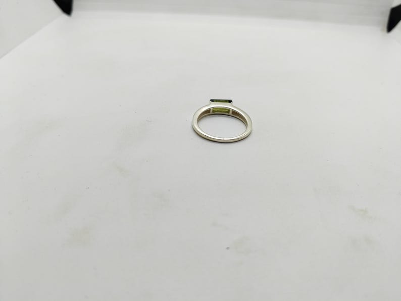 May include: A silver ring featuring a rectangular, light green gemstone. The ring band is a simple, polished silver. The gemstone is set horizontally across the top of the ring.