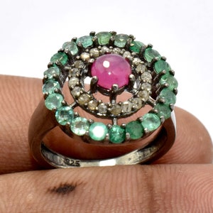 Könnte beinhalten: Silberring mit einem zentralen rosa Edelstein, umgeben von grünen Smaragden. Der Ring hat ein Doppel-Halo-Design mit einem Band aus kleineren Edelsteinen und einem strukturierten Silberband. Schmuck.