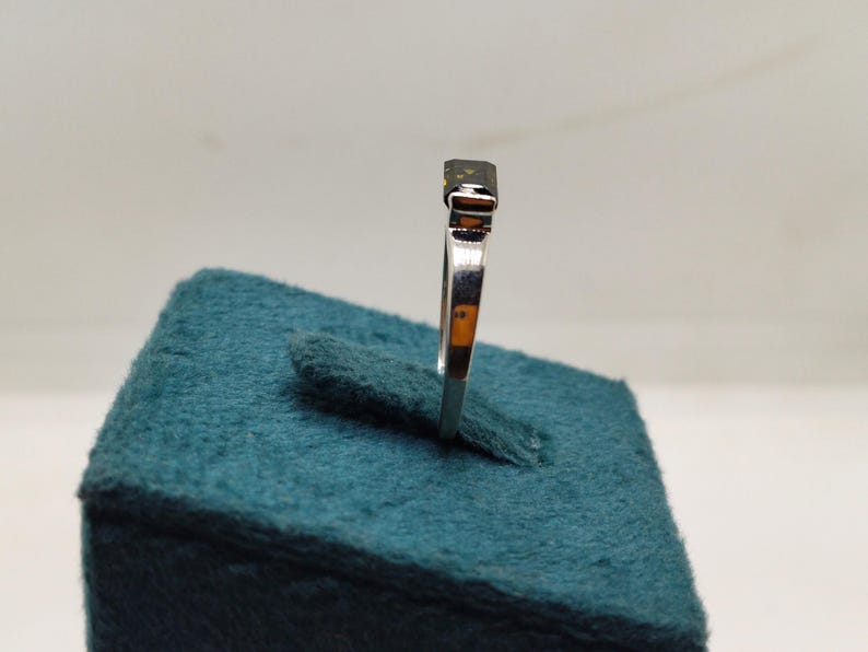 May include: A silver ring featuring a dark, rectangular gemstone. The ring is presented on a teal display. The band is slender and polished. The gemstone appears to be cut. The ring is angled to highlight its design.