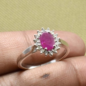 Könnte beinhalten: Ein silberner Ring mit einem großen ovalen Rubin, der von kleineren Diamanten umgeben ist.