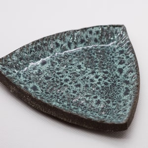 May include: A triangular ceramic dish with a speckled green and black glaze. The dish has a rough, textured surface.
