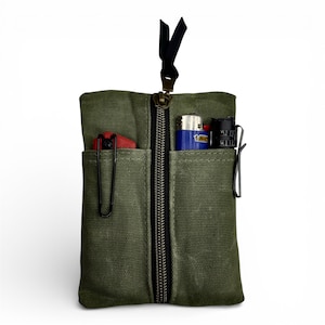 May include: Olive green canvas pouch with a black zipper and multiple pockets. The pouch contains a red lighter, a blue BIC lighter, and a black lighter. A black ribbon is attached to the top.