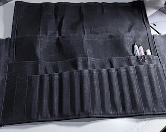 May include: A black canvas roll-up case with multiple pockets for holding pens, pencils, and other art supplies. The case is open and the pockets are visible.