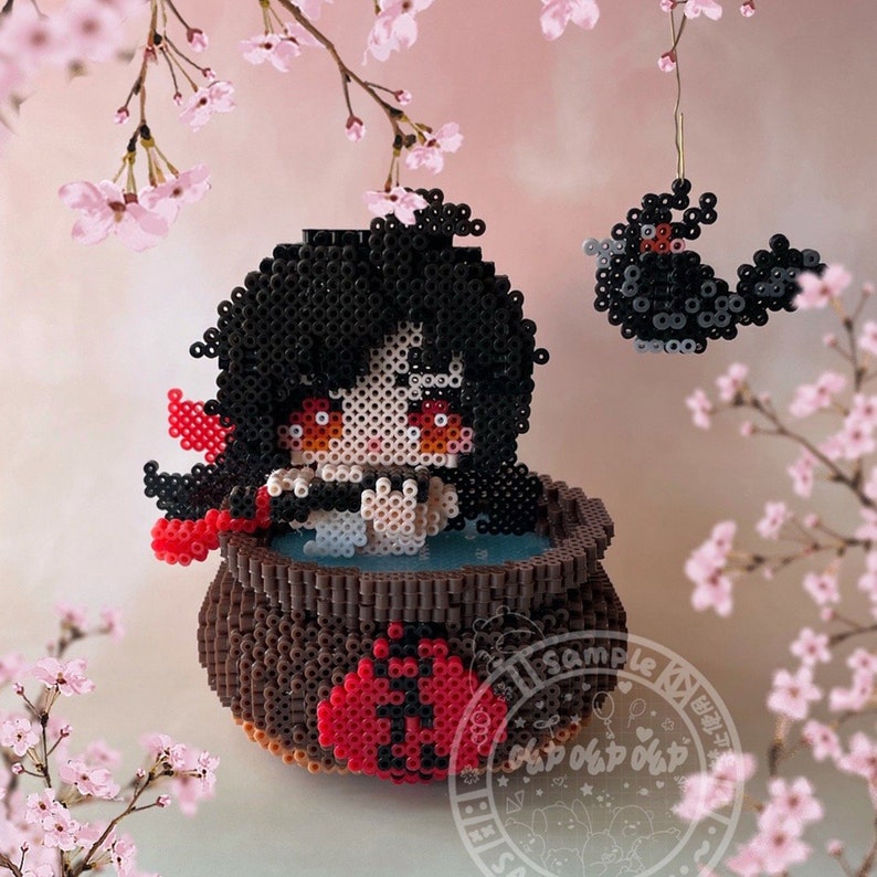May include: A beaded figure of a girl with black hair and red eyes, sitting in a brown pot with red and white accents. The figure is surrounded by pink cherry blossoms.