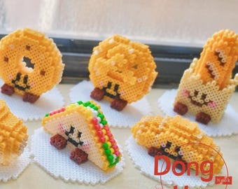 May include: A collection of handmade, pixelated food items, including a taco, french fries, and a donut. Each item has a smiling face and small brown feet. The items are arranged on white, scalloped-edge coasters.