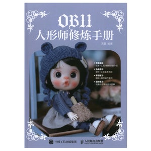 Puede incluir: Una portada de libro con fondo azul y una muñeca que lleva un gorro azul tejido con orejeras y un suéter azul. El título del libro es "OB11 人形师修炼手册" que se traduce como "Manual de entrenamiento para fabricantes de muñecas OB11".