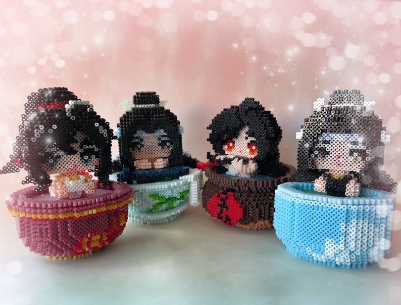 May include: Four colorful ceramic teacups with cartoon characters made of black and white beads. Each character is sitting in a teacup with a different color and design.