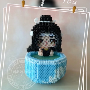 May include: A blue and white bead sprite of a person with black hair and a black swimsuit sitting in a blue pool. The bead sprite is surrounded by a white border.