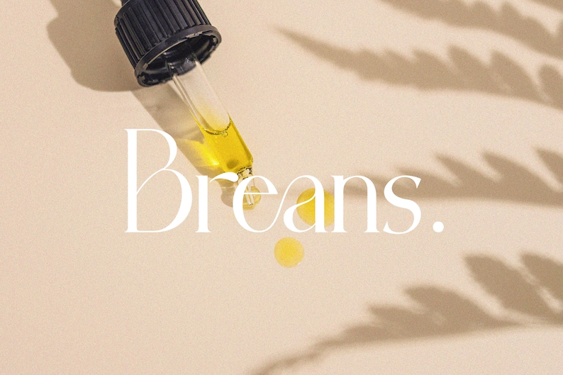 May include: A dropper bottle with a clear glass dropper and a black cap. A drop of yellow liquid has been dispensed onto a beige surface. The word "Breans." is written in white text on the surface.