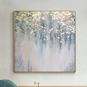May include: Abstract painting with gold and blue accents on a white canvas. The painting is framed in a gold frame and is hanging on a white wall.