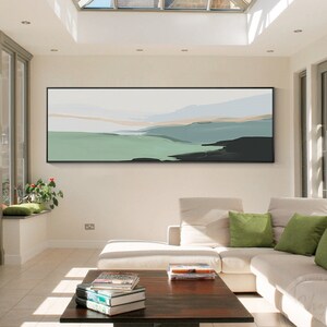 Puede incluir: Un sofá seccional blanco con almohadas verdes en una sala de estar moderna con una gran pintura abstracta de paisaje en la pared y una mesa de café de madera con libros encima.