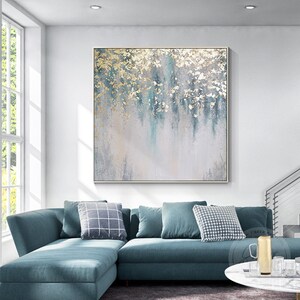 Op de afbeelding: Abstract schilderij met gouden en blauwe accenten op een canvas. Het schilderij is ingelijst en hangt aan een witte muur boven een blauwe hoekbank.