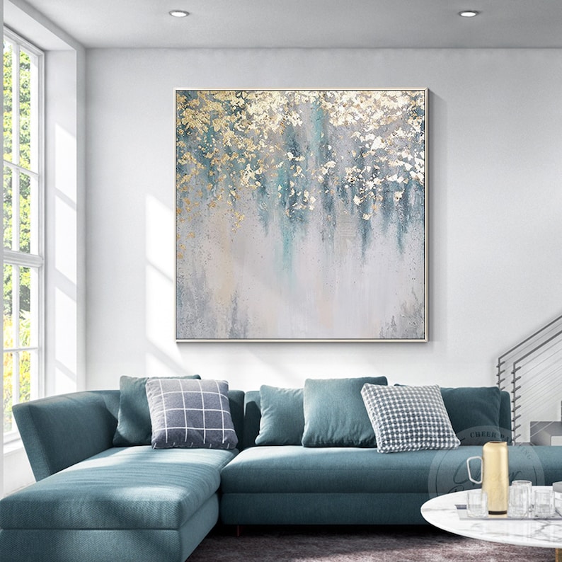 Op de afbeelding: Abstract schilderij met gouden en blauwe accenten op een canvas. Het schilderij is ingelijst en hangt aan een witte muur boven een blauwe hoekbank.