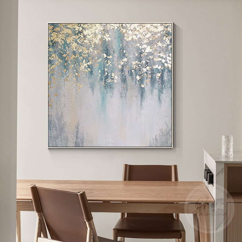 Op de afbeelding: Abstract schilderij met een witte achtergrond en blauwe en gouden accenten. Het schilderij heeft een textuur met gouden blad accenten.
