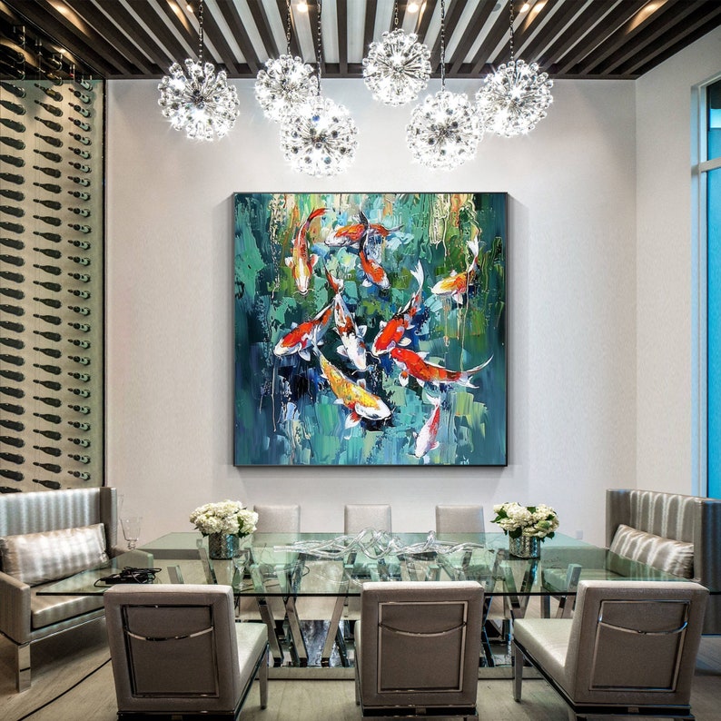 May include: An oil painting of koi fish in a pond hangs above a glass dining table. The painting features orange, yellow, and white fish against a green and blue background. The dining room has a modern design with crystal chandeliers.