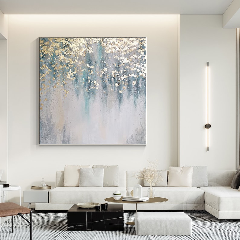 Op de afbeelding: Abstract schilderij met een witte achtergrond en blauwe en gouden accenten. Het schilderij heeft een textuur en is ingelijst in een dun, wit frame.