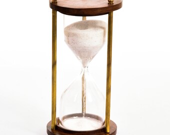 May include: An hourglass with a wooden top and base, connected by brass-colored metal rods. The clear glass center holds white sand. The wooden components are a dark brown color, and the hourglass is set against a white background.