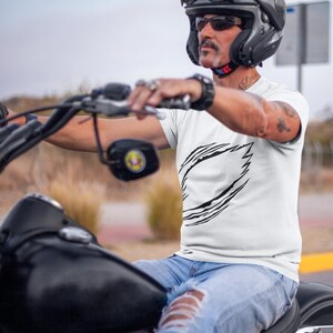 May include: A man wearing a white t-shirt with a black graphic design of a stylized lightning bolt. He is riding a black motorcycle and wearing a black helmet with a tinted visor.