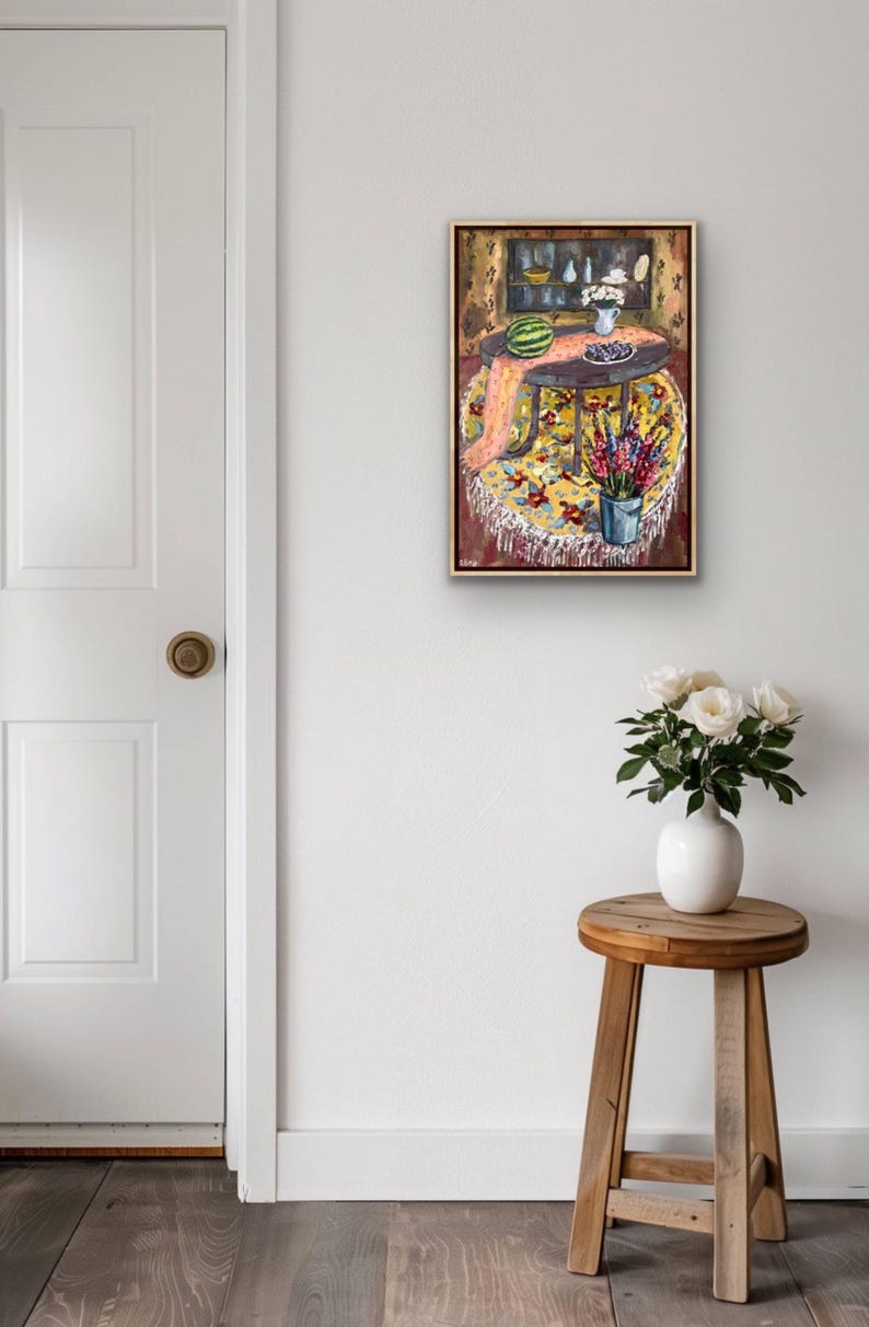 May include: An oil painting depicts a round table with a yellow floral tablecloth, a watermelon, and a vase of flowers. A small wooden stool holds a white vase with white roses. A white door is on the left.