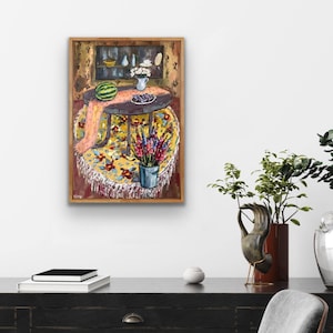 May include: A framed painting depicts a still life scene. A round table is covered with a yellow floral tablecloth and a pink scarf. A watermelon, blueberries, and a vase of flowers are on the table. A bucket of flowers sits below the table.