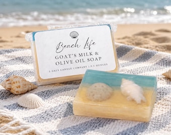 May include: Beach Life Goat's Milk & Olive Oil Soap, 3.5 ounces, with a seashell design. The soap is on a striped towel with seashells. The packaging has the text "Beach Life" and "3 Gals Candle Company".