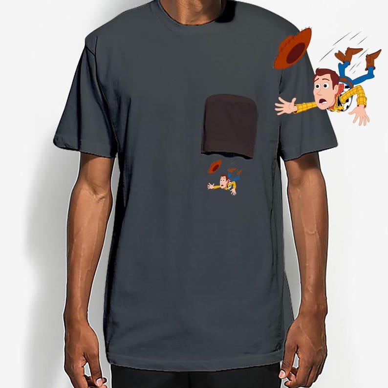 May include: Dark gray t-shirt featuring a cartoon illustration of a cowboy character falling from a pocket. The cowboy is wearing a yellow shirt, blue jeans, and a brown hat. The pocket is brown.