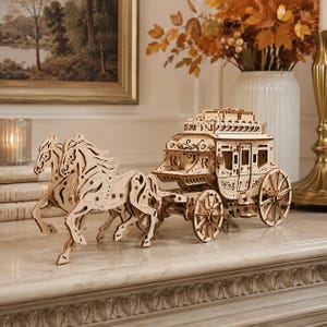 May include: A light-colored wooden model of a horse-drawn carriage featuring two horses pulling a detailed coach with intricate cut-out patterns, spoked wheels, and a roof structure, constructed from interlocking laser-cut wooden pieces.