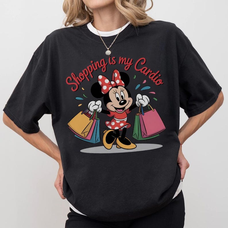 Puede incluir: Camiseta negra con Minnie Mouse sosteniendo bolsas de compras. Minnie lleva un vestido rojo con lunares blancos y un lazo a juego. El texto "Shopping is my Cardio" est&aacute; escrito en rojo sobre el personaje.