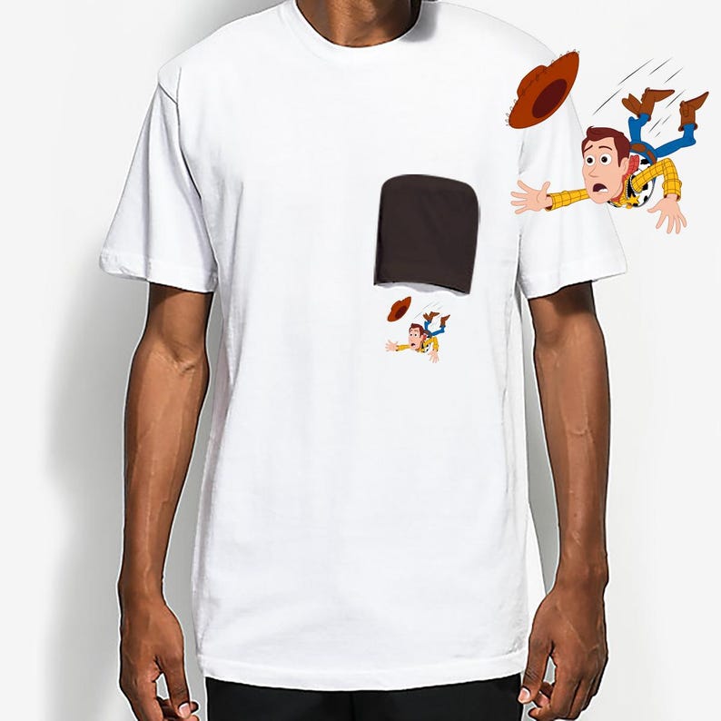 May include: White t-shirt featuring a cartoon illustration of a character falling out of a pocket. The character is wearing a cowboy hat, yellow shirt, blue jeans, and brown boots. The pocket is dark brown.