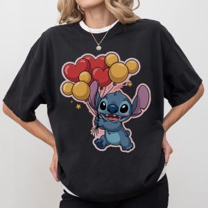 May include: Black t-shirt featuring a cartoon character holding heart and round balloons. The character is blue with large ears and a friendly expression. The balloons are red and yellow, with small stars in the background.