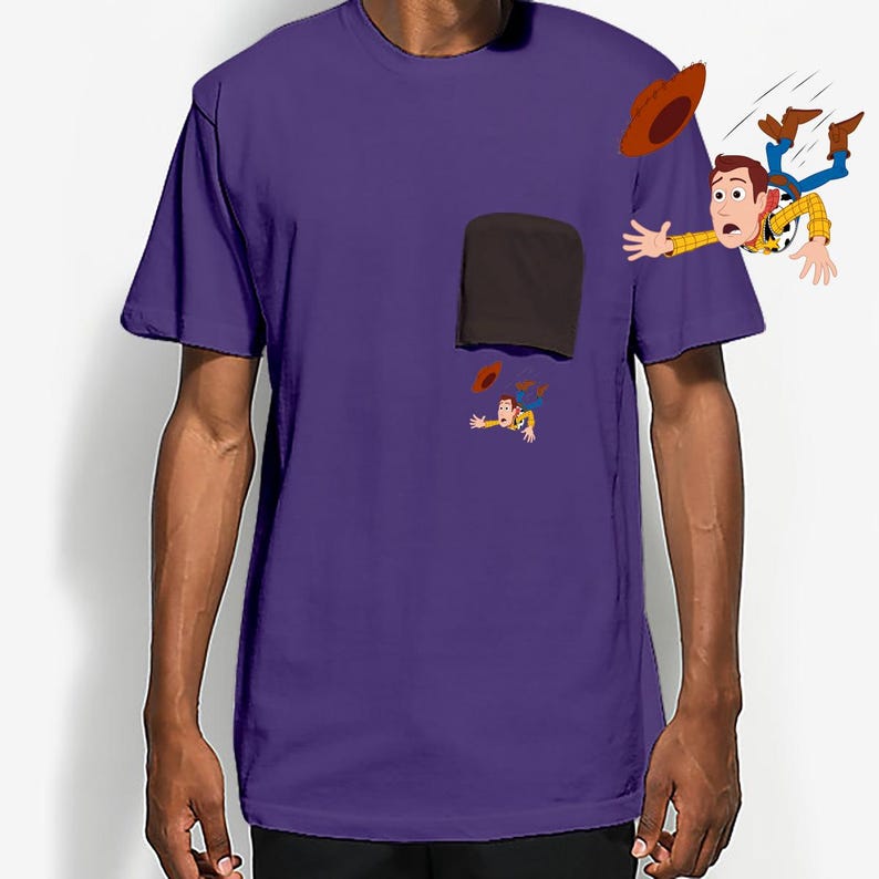 May include: Purple t-shirt featuring a cartoon graphic of a character falling from a pocket. The character is wearing a cowboy hat, a yellow plaid shirt, blue jeans, and brown boots. The shirt has a brown pocket.