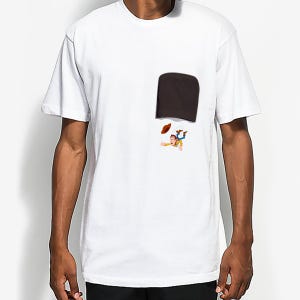 May include: White t-shirt featuring a dark brown pocket with a cartoon illustration of a character falling out of the pocket. The character is wearing a cowboy hat and a yellow shirt.