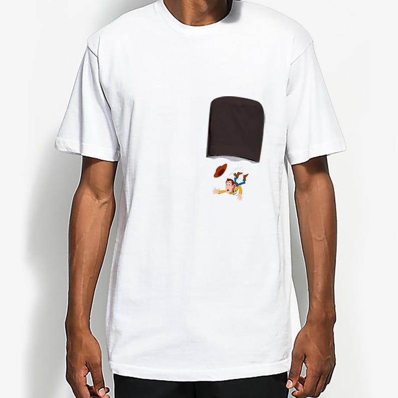 May include: White t-shirt featuring a dark brown pocket with a cartoon illustration of a character falling out of the pocket. The character is wearing a cowboy hat and a yellow shirt.
