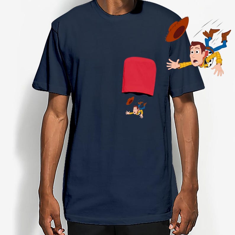May include: Navy blue t-shirt featuring a red pocket and a cartoon illustration of a character falling. The character is wearing a cowboy hat, a yellow shirt, and blue jeans. The design is on the front of the shirt.