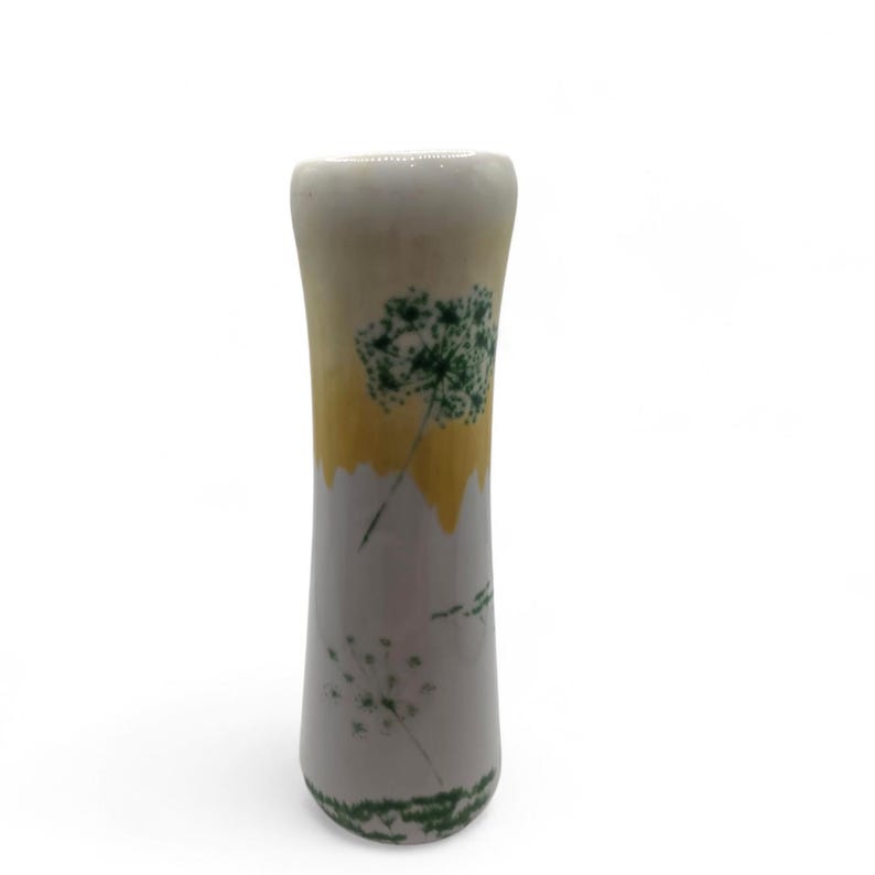 May include: A ceramic vase with a white, yellow, and gray color scheme. The vase features green dandelion designs. The vase has a cylindrical shape and is suitable for displaying flowers or as a decorative item.