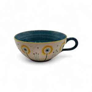 May include: A ceramic teacup with a wide, rounded bowl and a dark blue handle. The interior is dark blue, and the exterior is off-white with yellow and blue floral designs. A thin yellow line accents the rim.