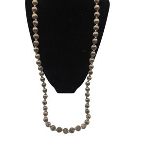 May include: A long necklace featuring a continuous strand of round, grey, textured beads alternating with small, smooth, gold-toned spacer beads. The beads are arranged in a single, uniform loop, creating a classic and symmetrical design.